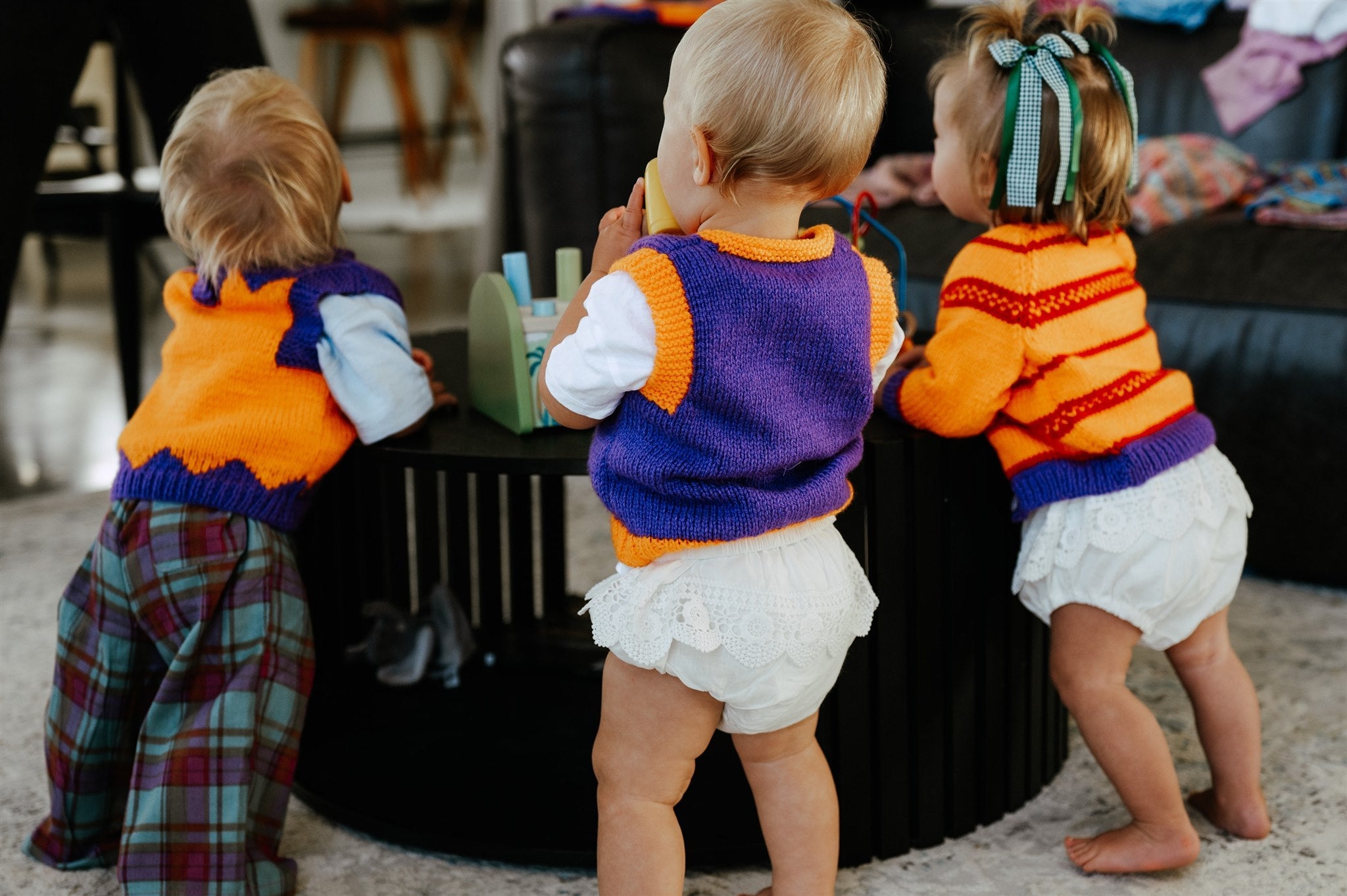 three kids wearing orange purple and red knit vests and cardigans