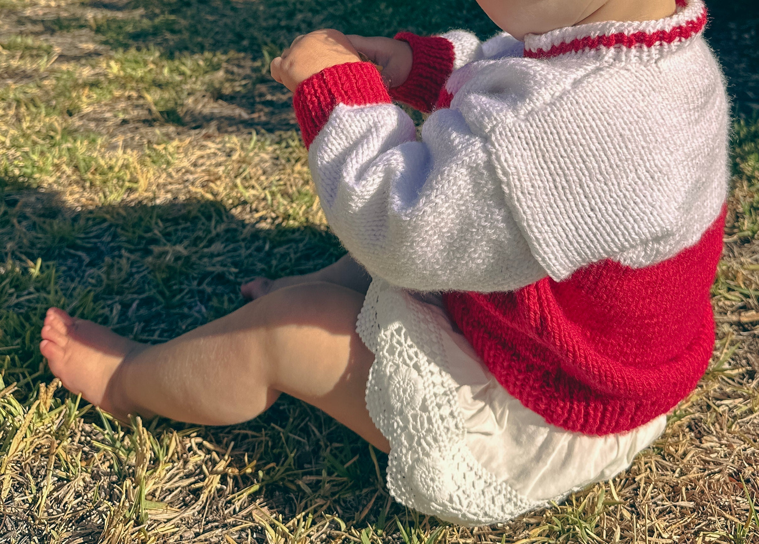baby girl in red & white handmade knit jumper sitting on grass outdoors