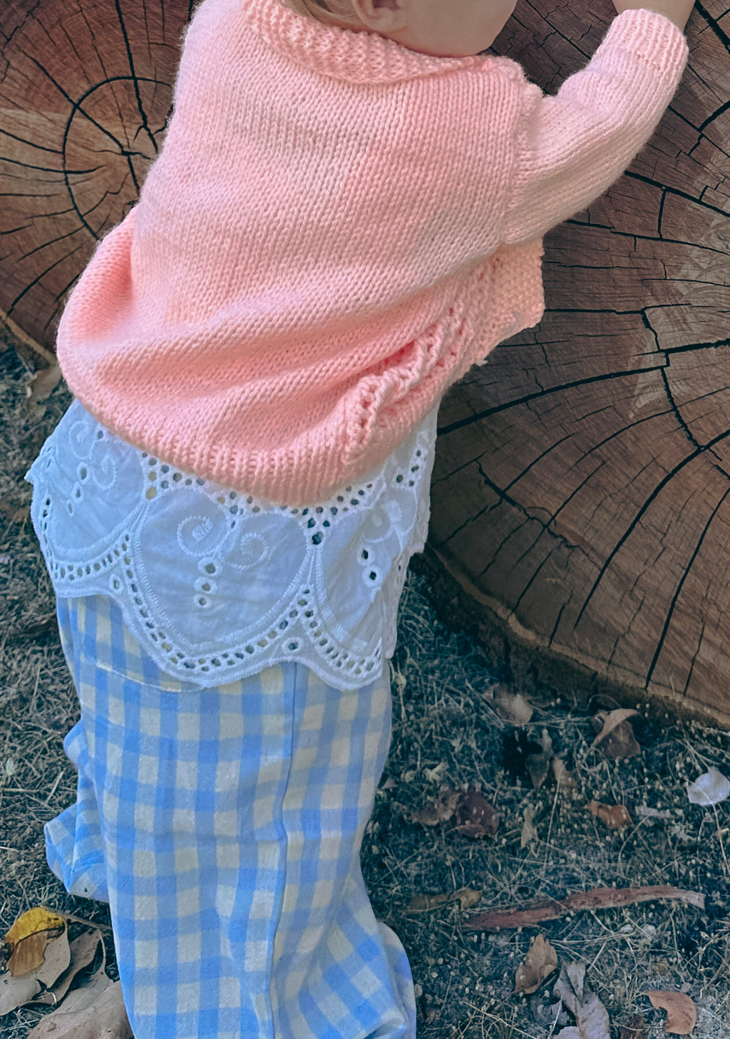 toddler standing in front of log in handmade orange knit cardigan 