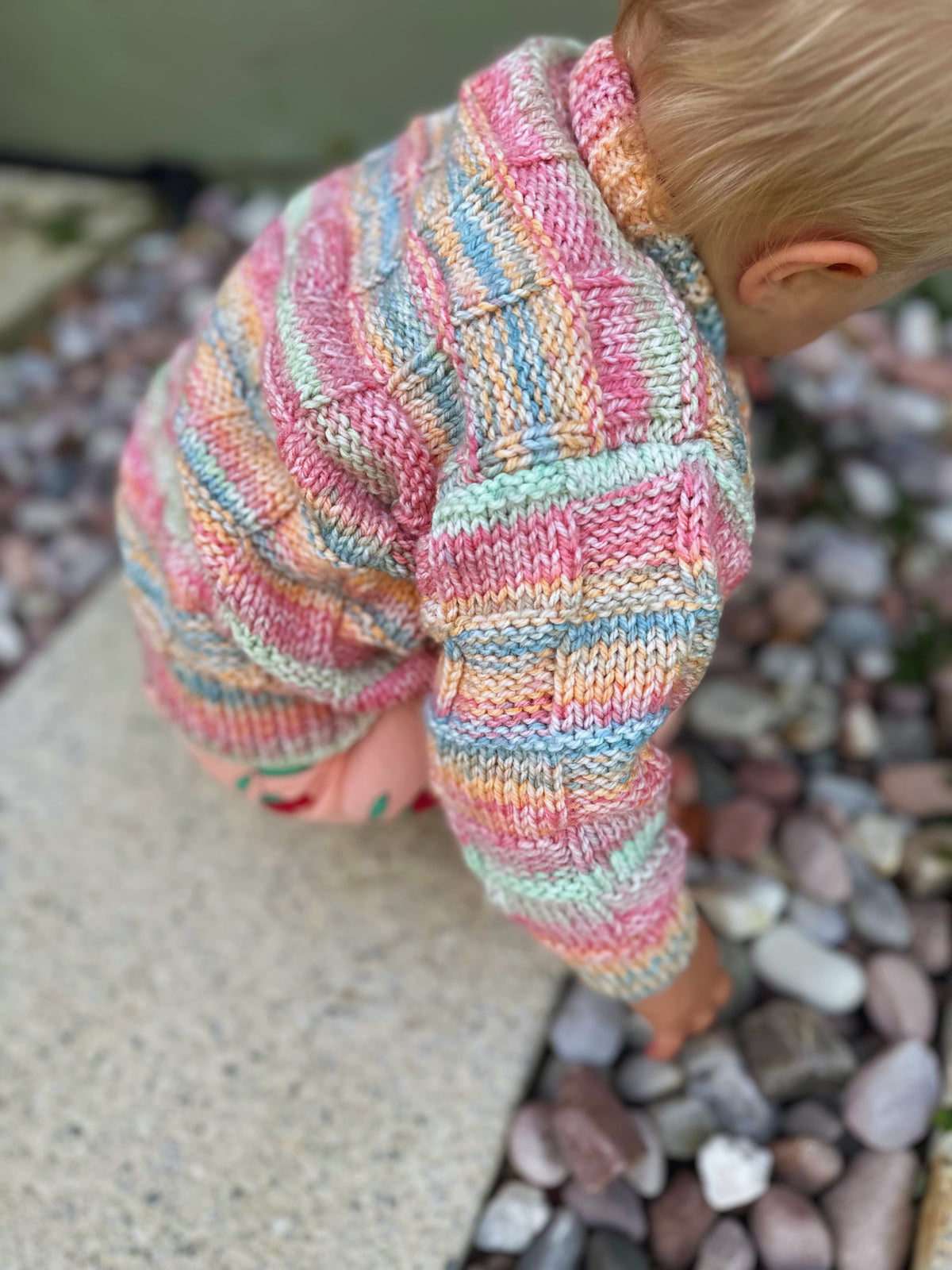 Child wearing a colorful knitted outfit on a stone surface