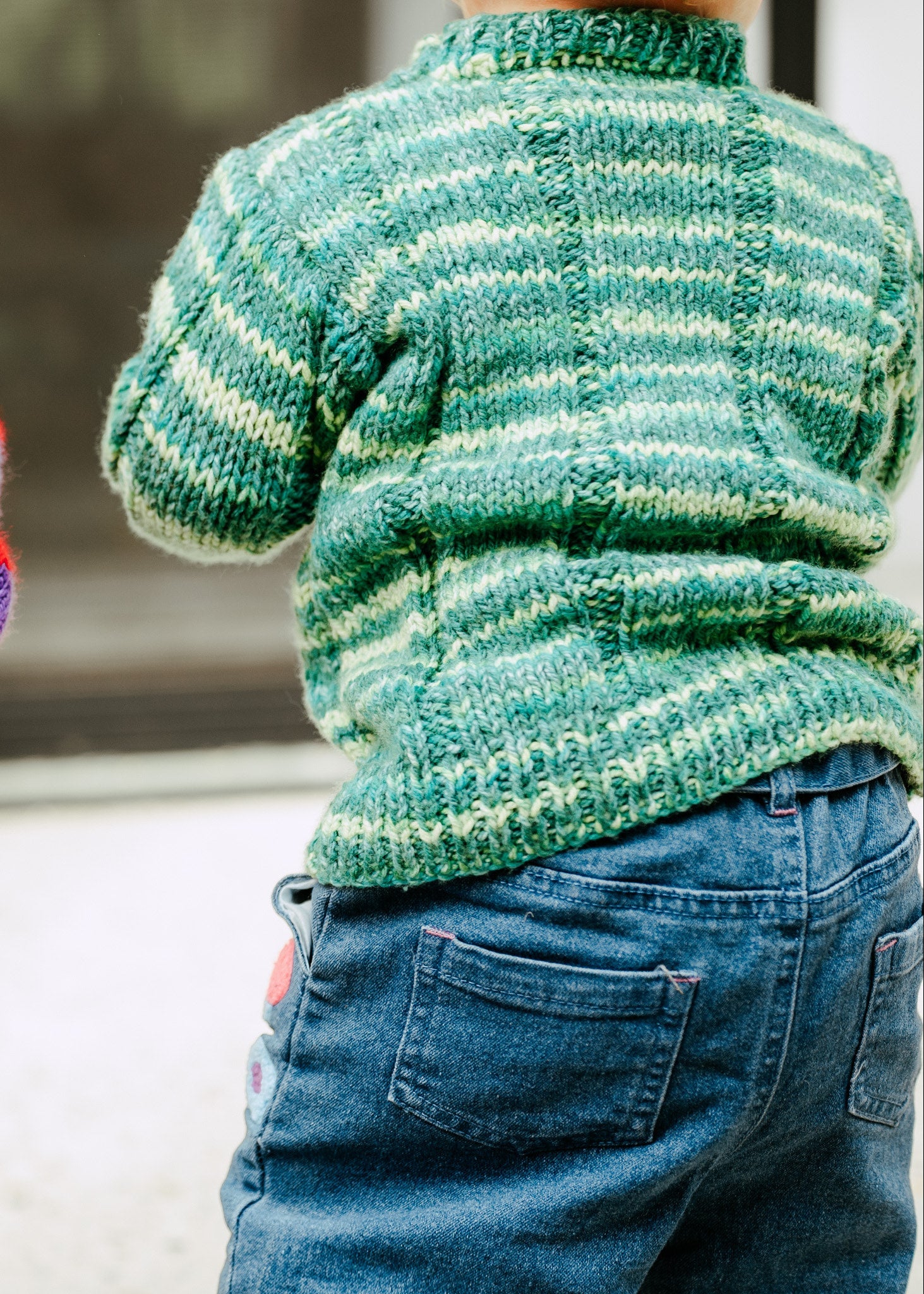 A child in a green striped knitted sweater with blue jeans