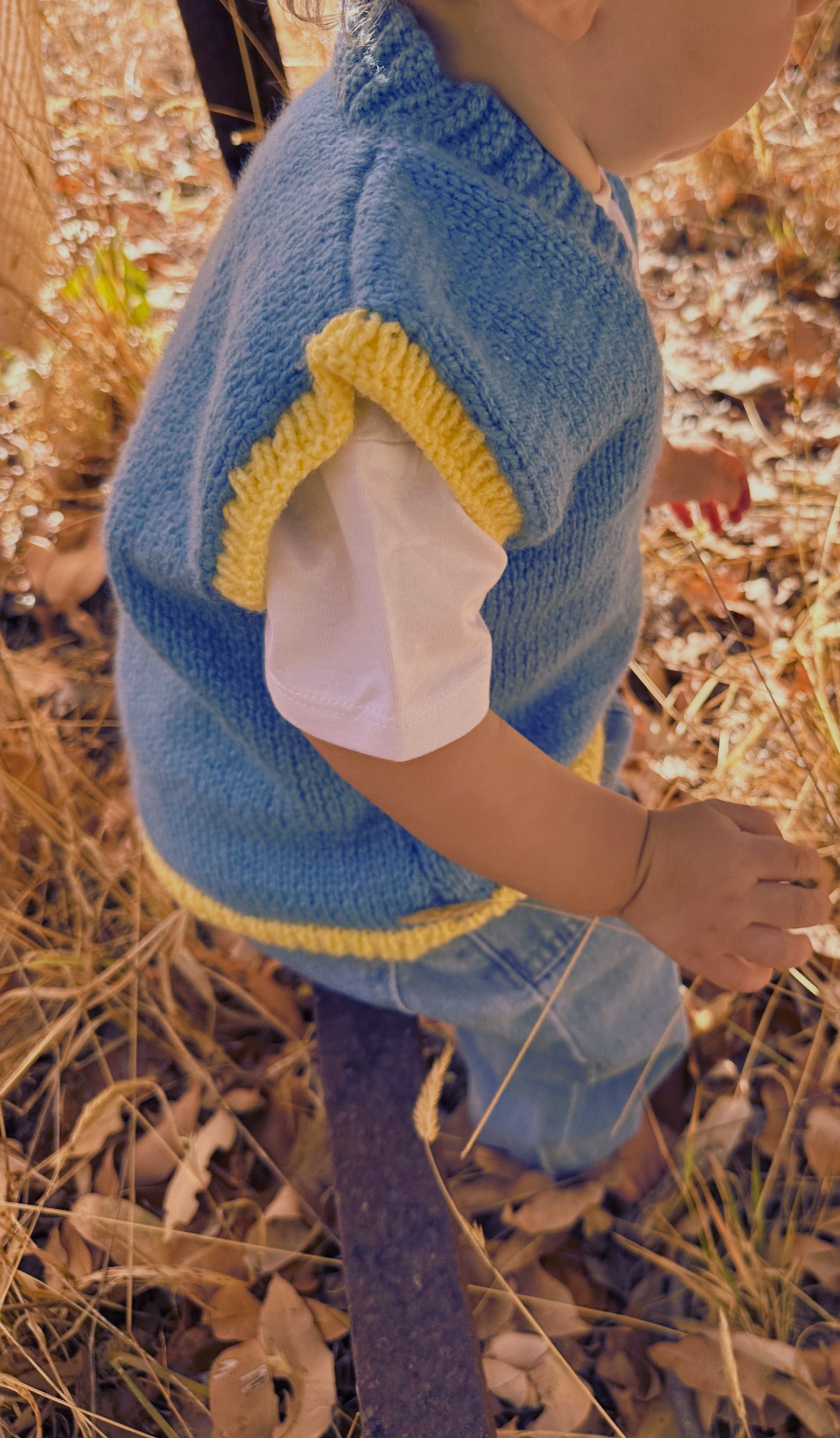 Child wearing a blue knitted vest with yellow trim in a natural setting
