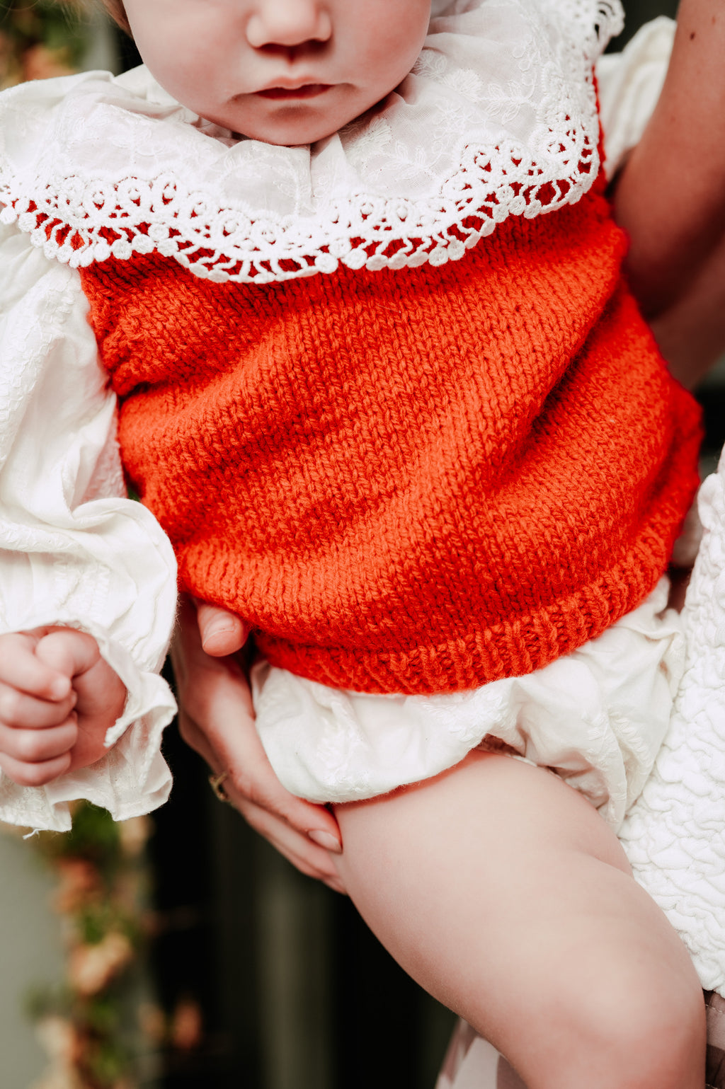 Baby wearing a red knitted outfit with white ruffled details