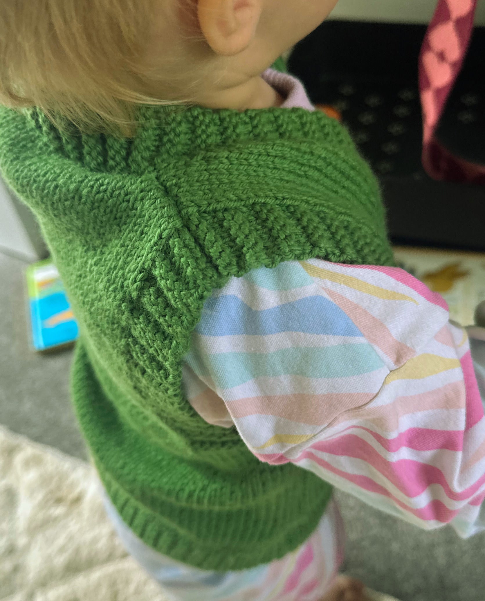 Close-up of a green knitted sweater on a girl with a colourful romper.