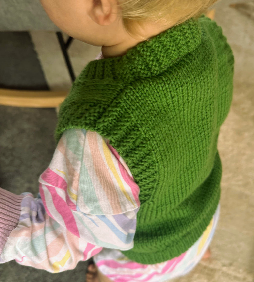 Child wearing a green knitted sweater with colorful romper