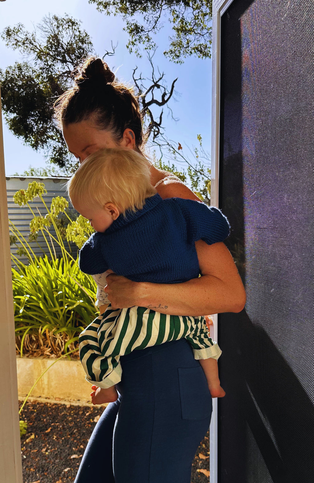 Woman holding a child outdoors with trees and a building in the background