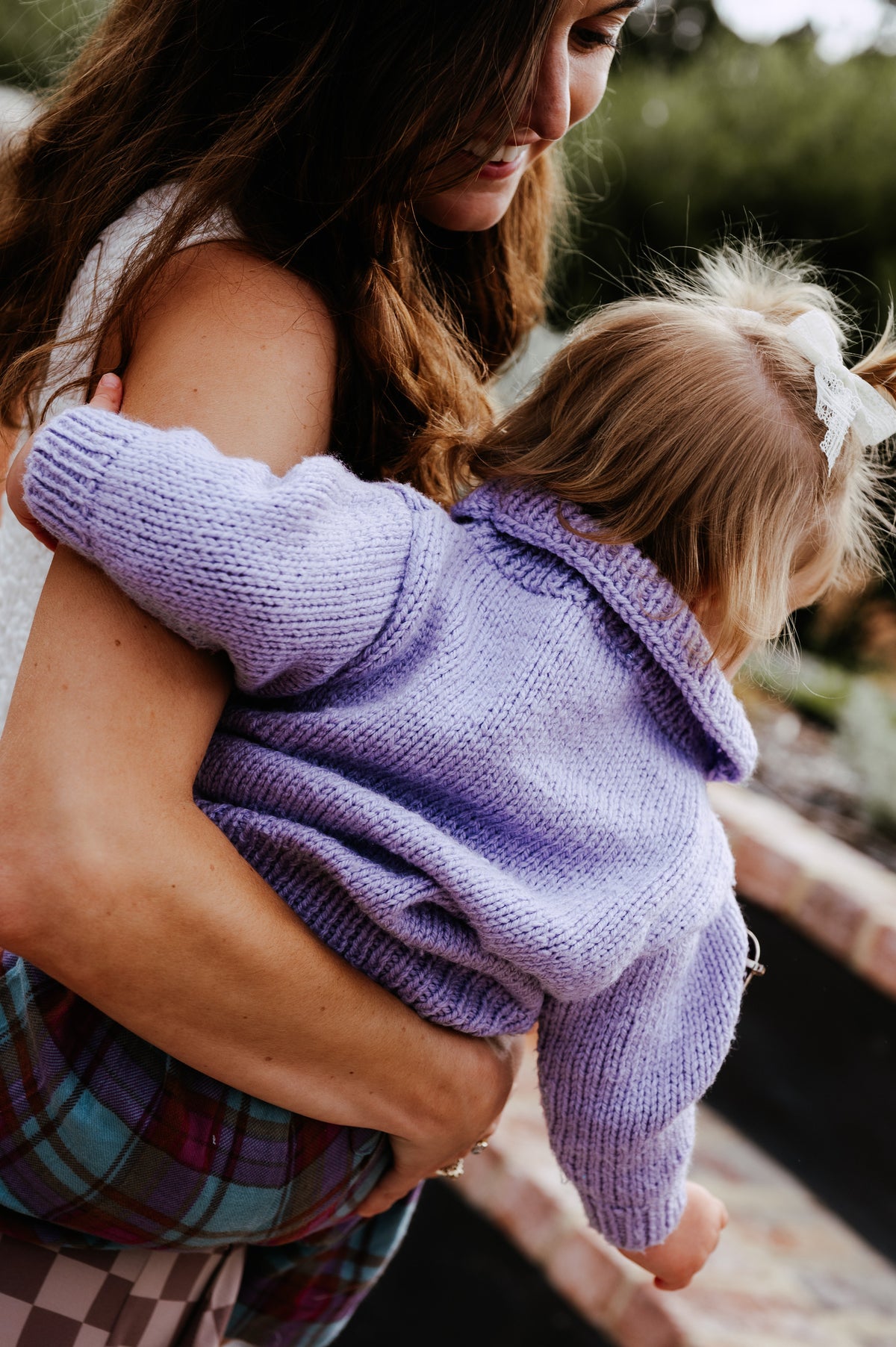 Woman holding a child wearing a purple sweater outdoors