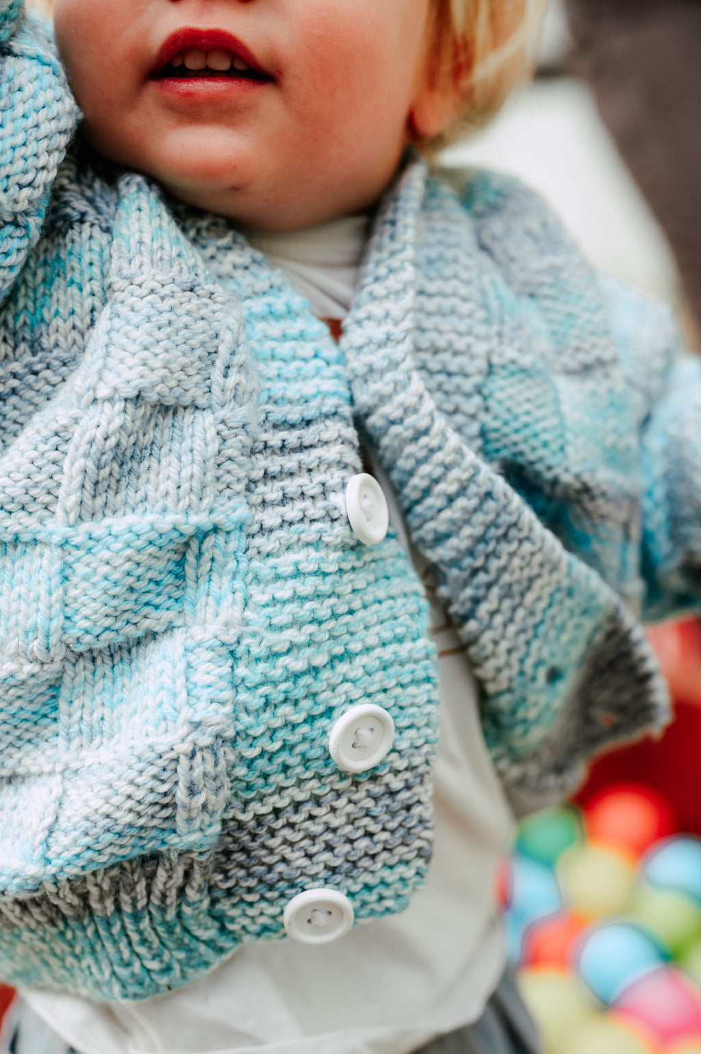 Close-up of a child wearing a blue knitted cardigan with buttons.