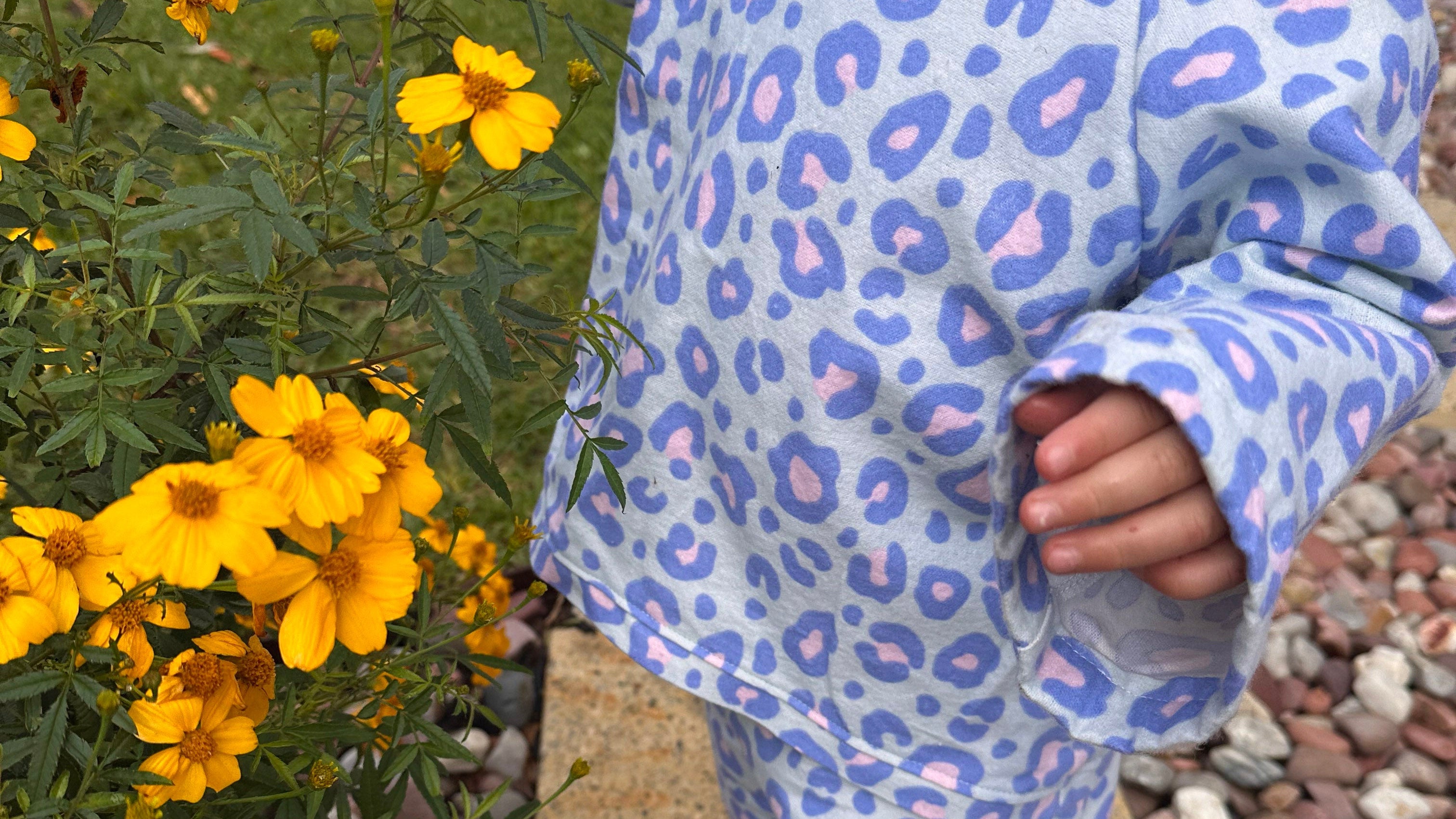 Child in a blue leopard print outfit standing next to yellow flowers