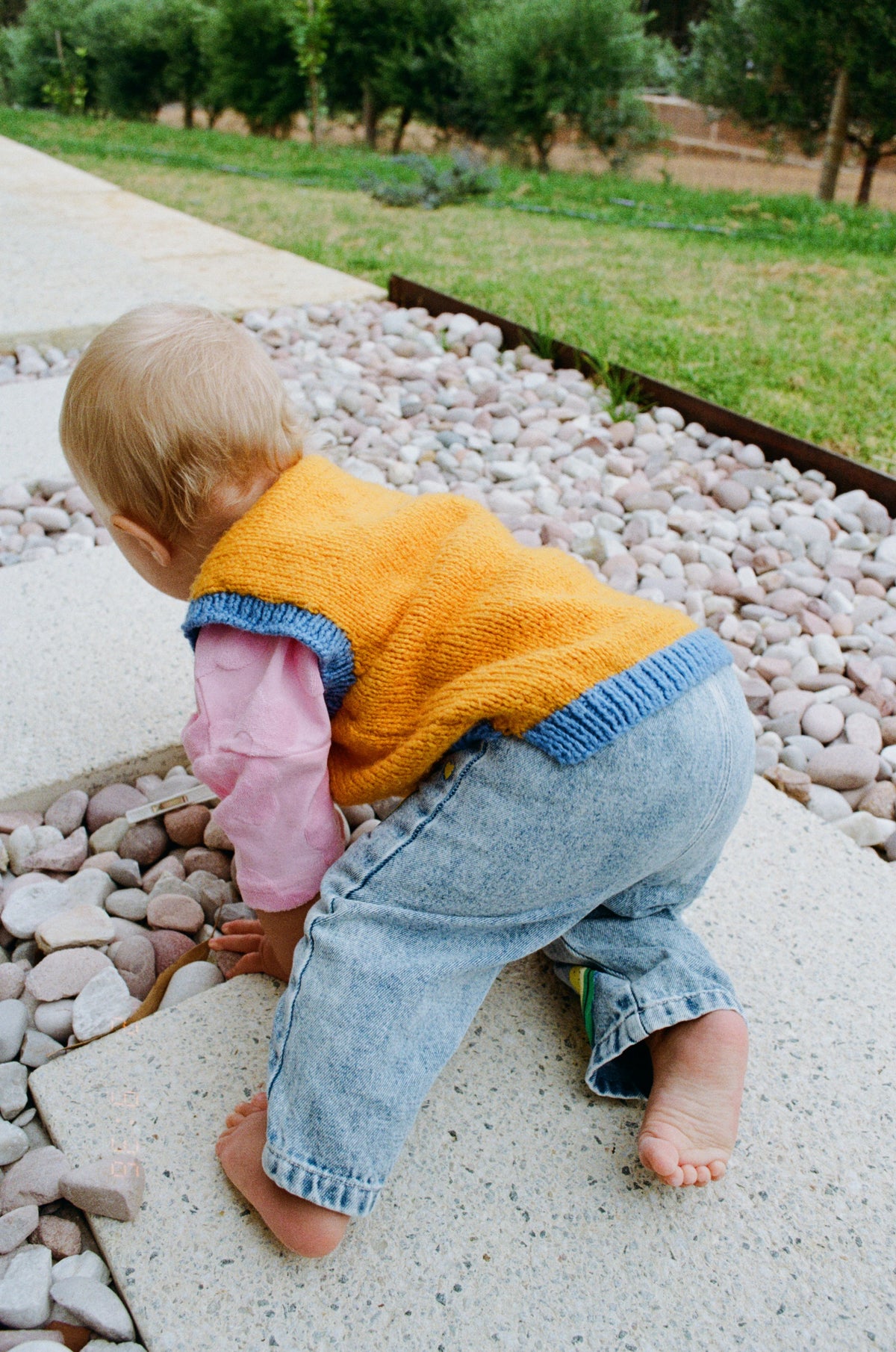Child in orange sweater and blue jeans crawling on a stone surface
