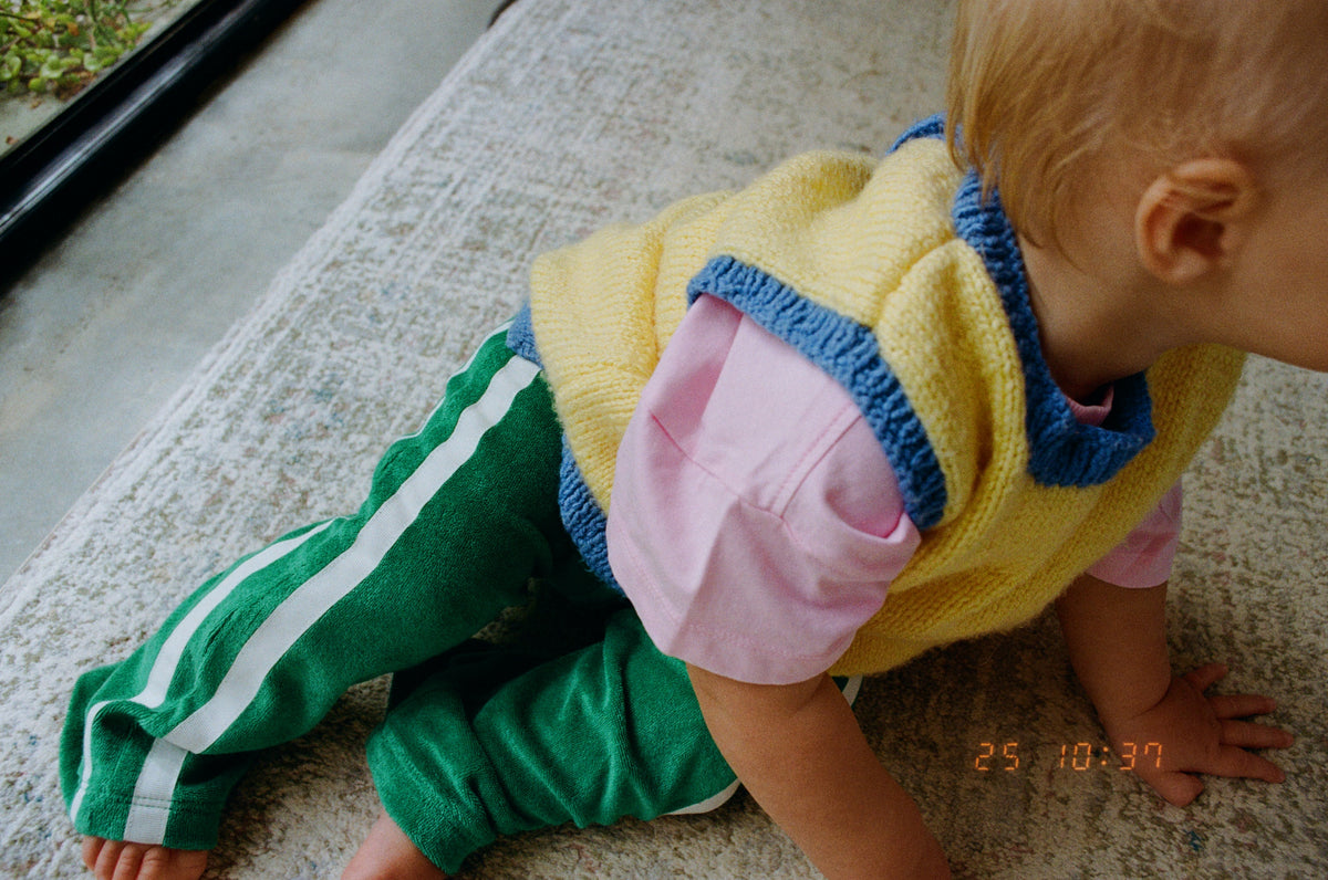 Child wearing a yellow sweater and green pants with white stripes on a carpeted floor.