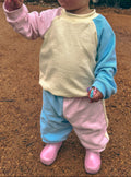 Child wearing a colorful outfit with pink, blue, and yellow colors standing on a dirt ground in margaret river