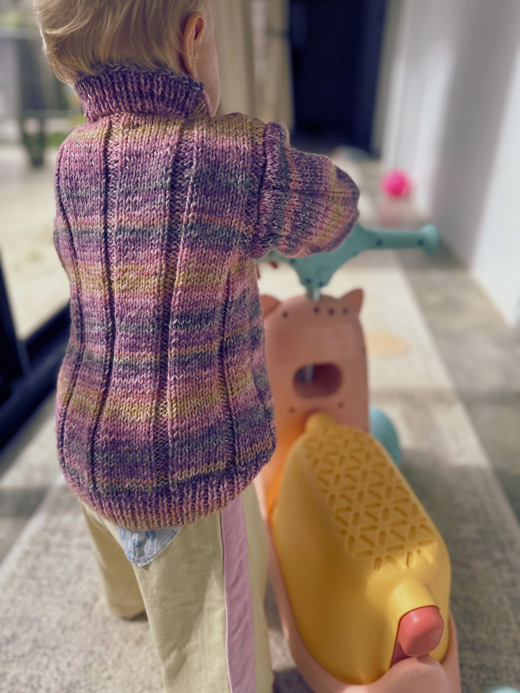 toddler in purple & yellow knitted jumper riding bike