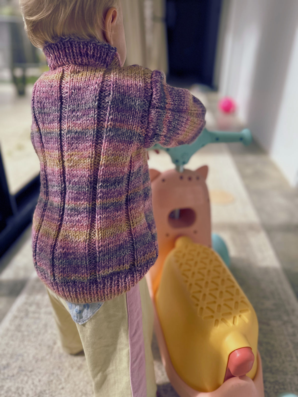toddler in purple & yellow knitted jumper riding bike