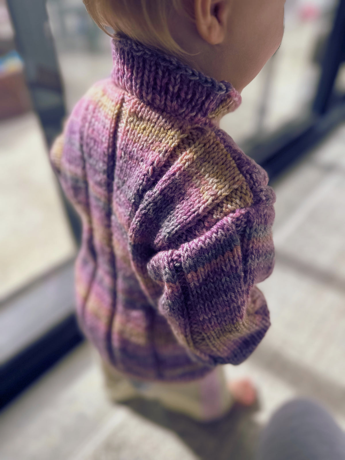 toddler in purple & yellow knitted jumper riding bike