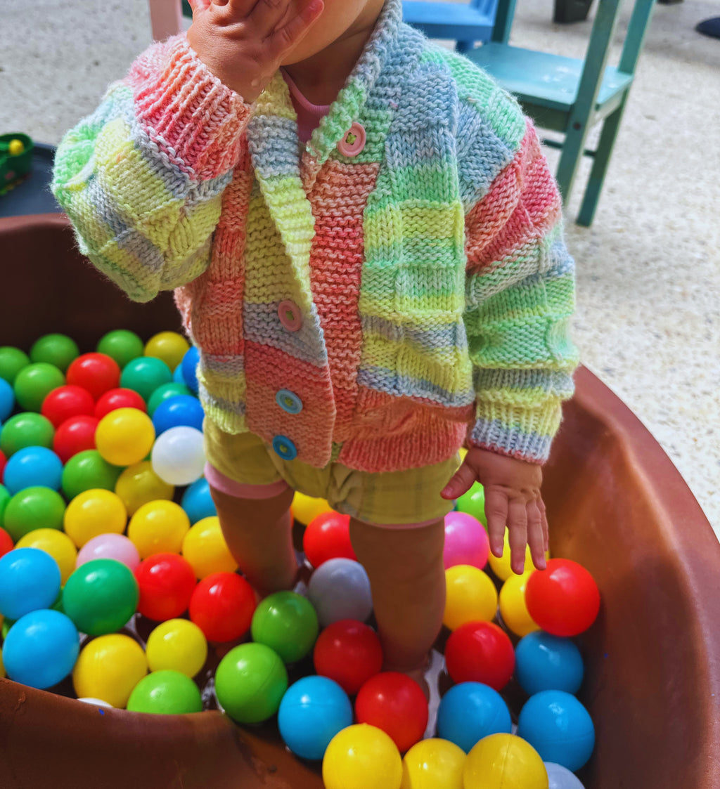 Child in a colorful striped sweater playing with colorful balls in a ball pit.