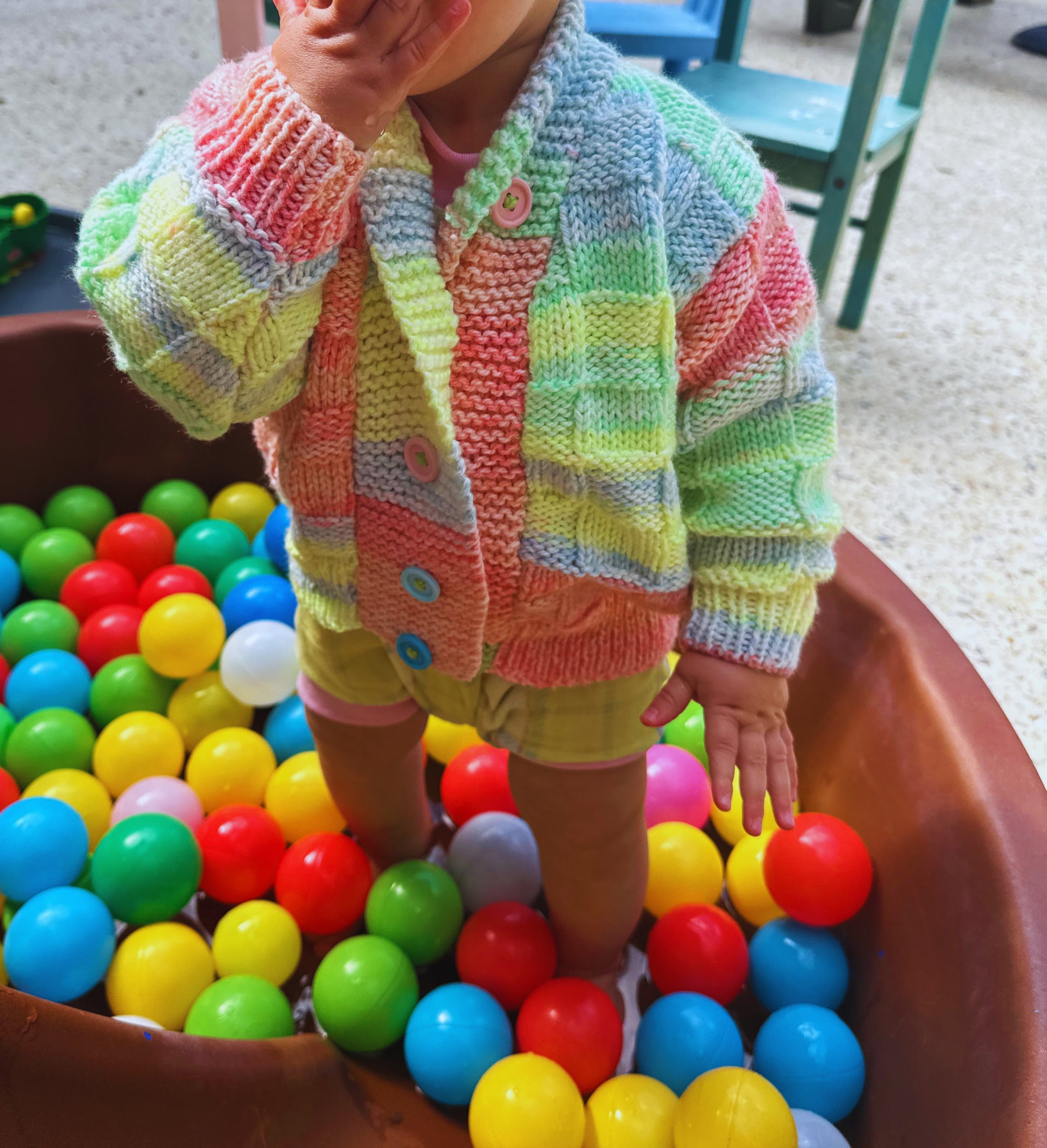 Child in a colorful striped sweater playing with colorful balls in a ball pit.