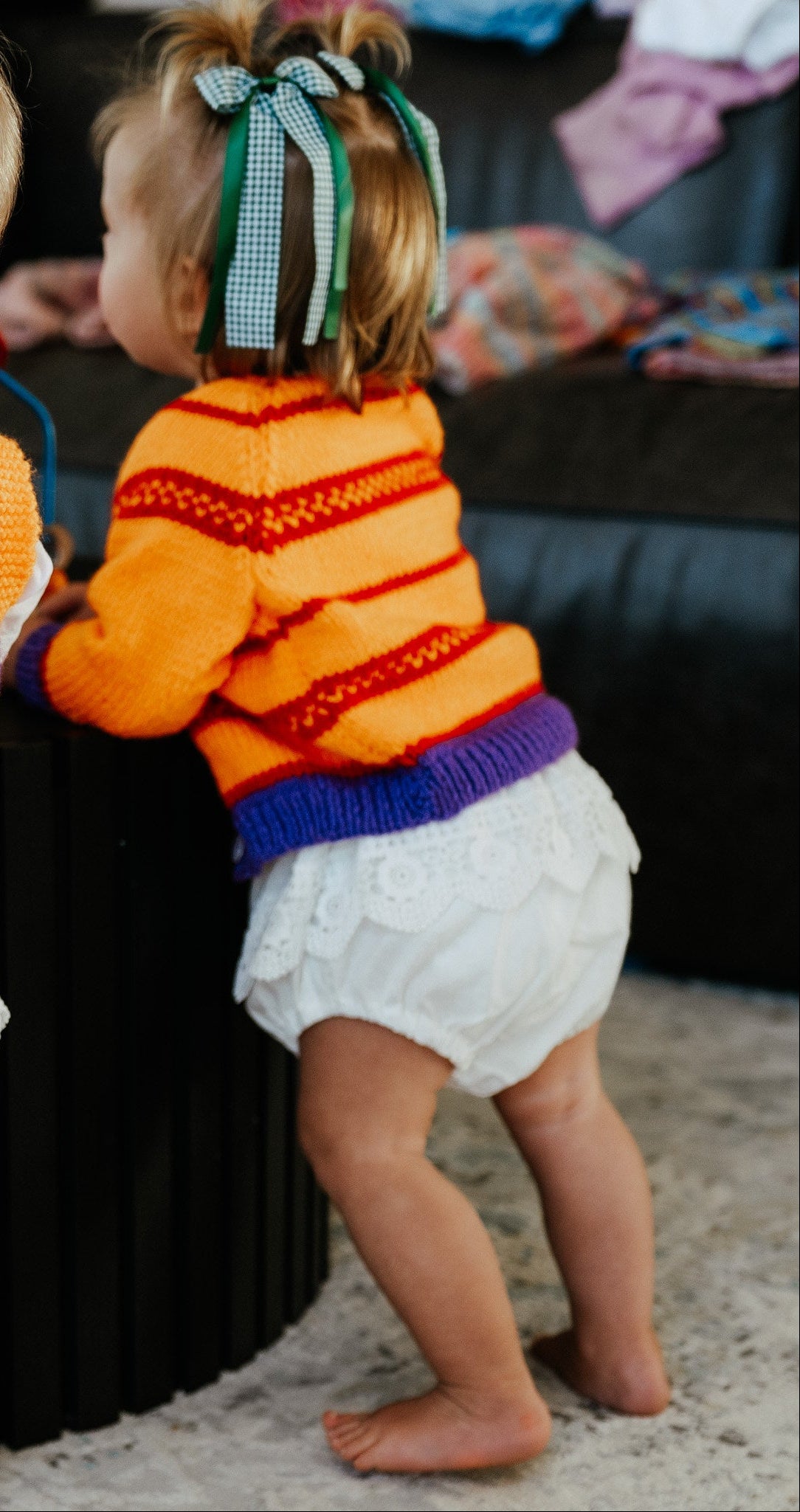 toddler wearing purple and orange knit cardigan with green bows in hair