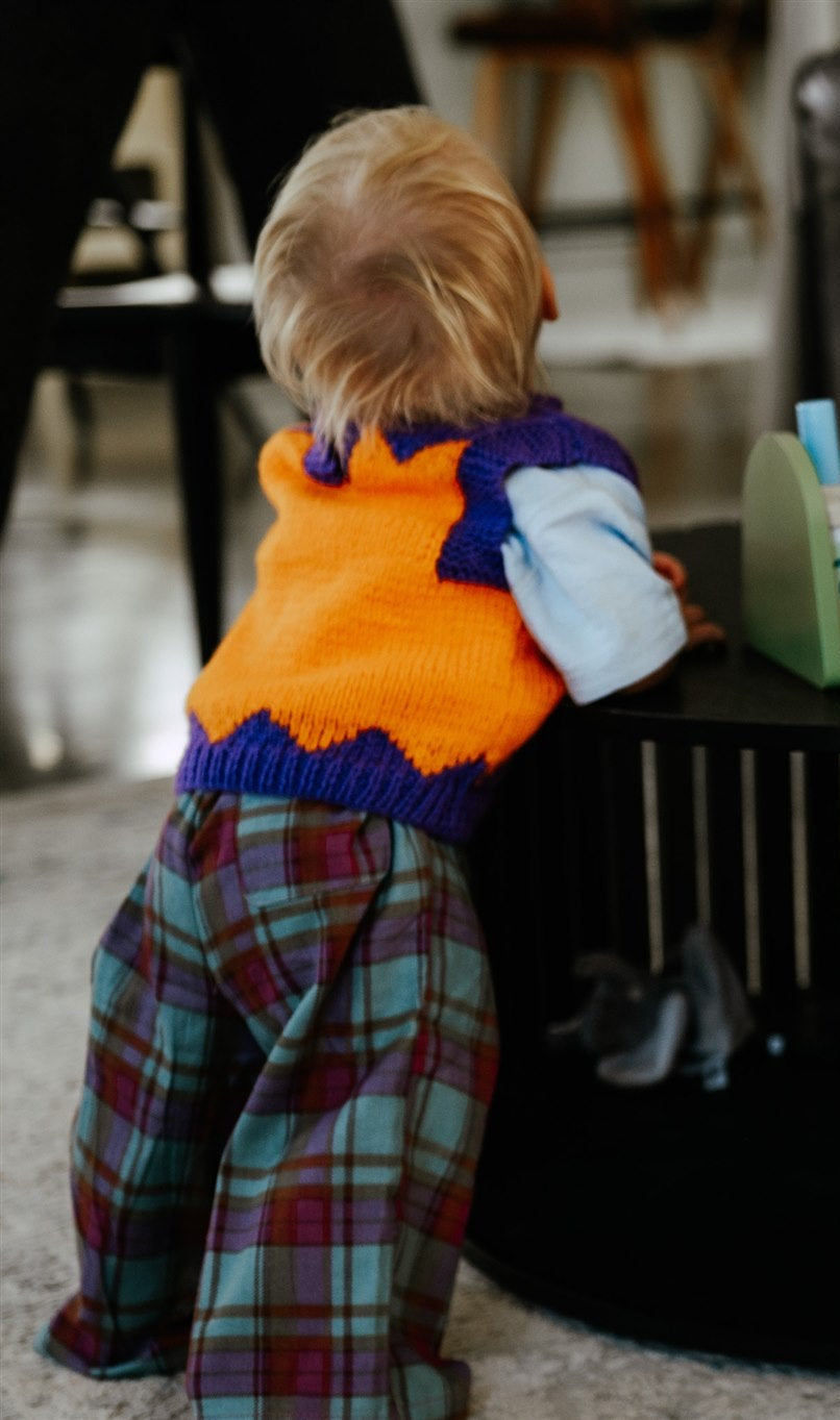 toddler wearing purple and orange knit vest an checked pants