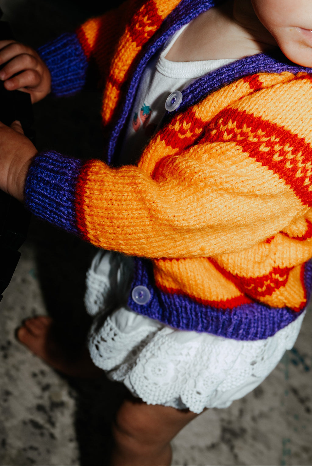toddler wearing purple and orange knit cardigan with green bows in hair