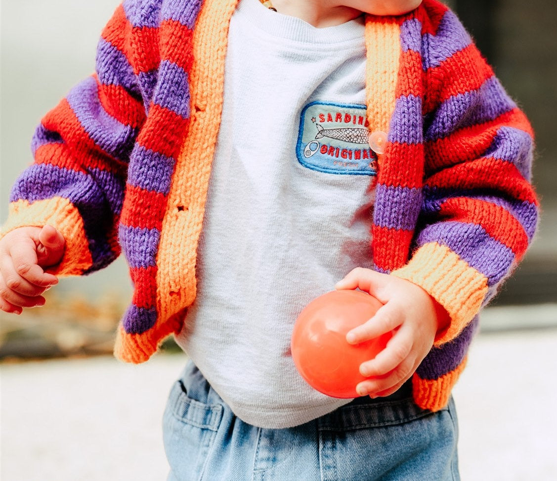 Two children playing outdoors, one holding a red ball, wearing colorful sweaters and jeans.